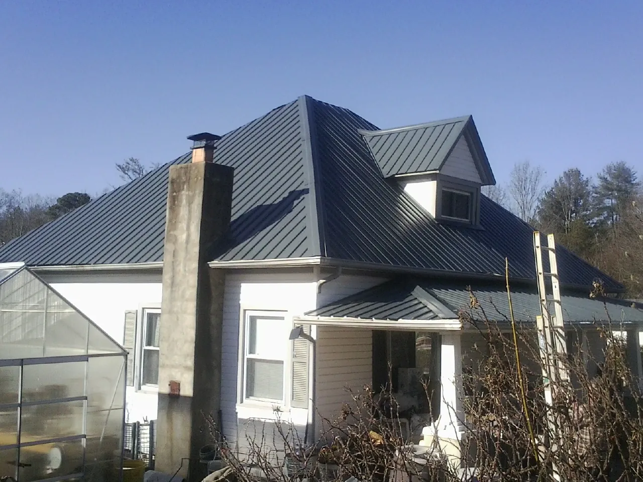 Dark blue standing seam metal roof on a white farmhouse with dormer — Slate & Tile Roof Repair by Roofing Brothers in Sunbright