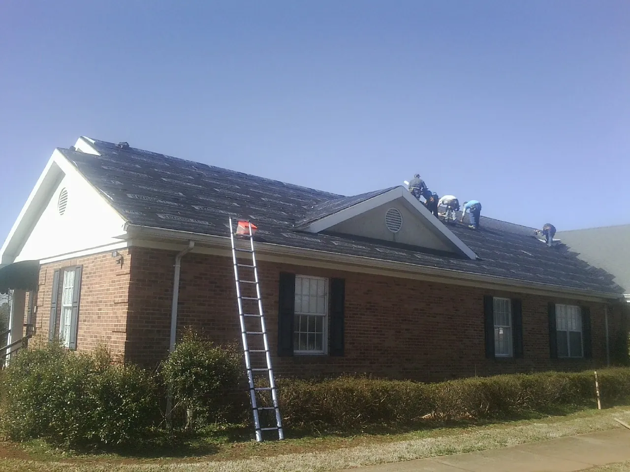 Crew tearing shingles off a brick ranch roof with a ladder set — Emergency Roof Repair work by our crew in Sunbright