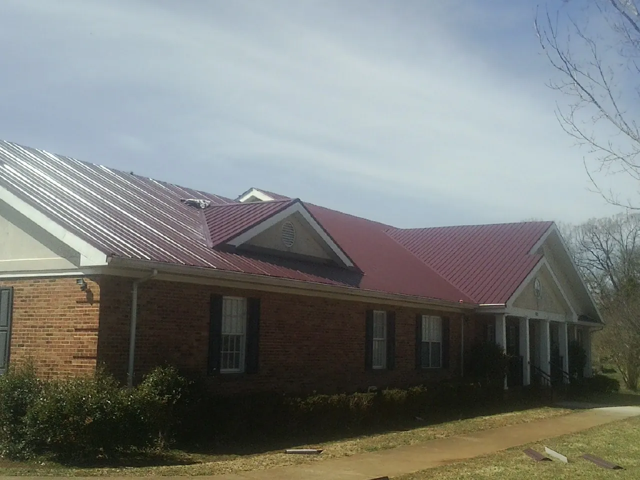 Red metal roof with gabled entries on a long brick building, from a Hail Damage Roof Repair job in Sunbright