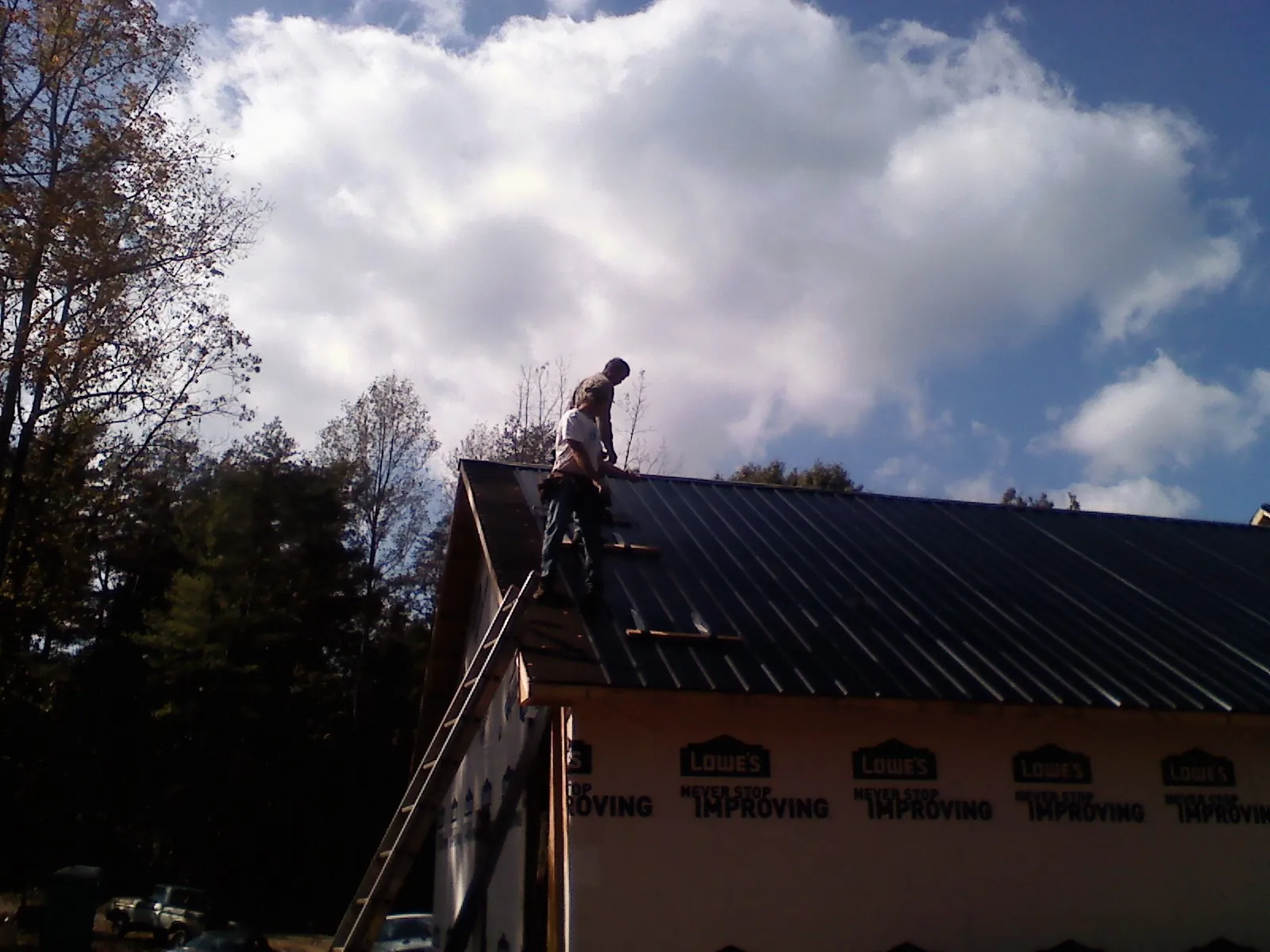 Roofer fastening dark metal panels high against a cloudy sky, from a Roof Inspection job in Sunbright