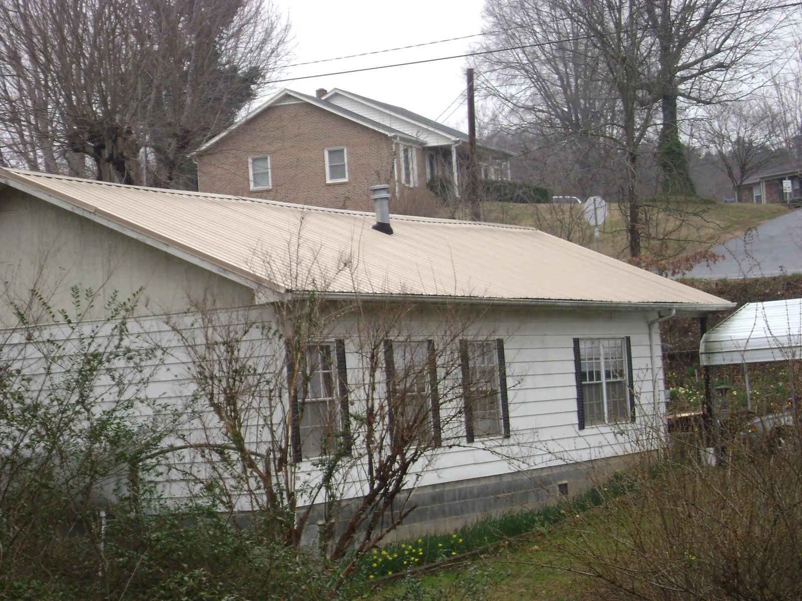 Tan metal roof on a white sided house set into a hillside — Commercial Roofing by Roofing Brothers in Sunbright