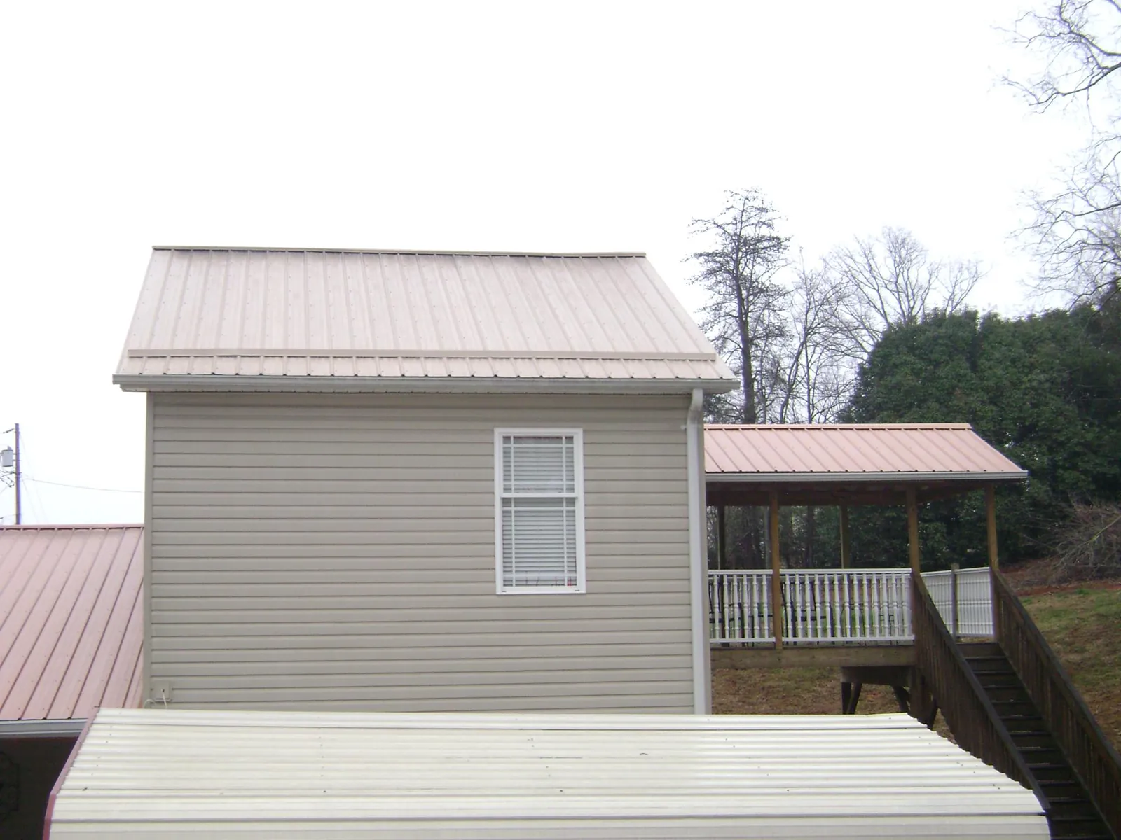 Tan metal roofs on a two story addition and attached porch, from a Roof Replacement job in Sunbright